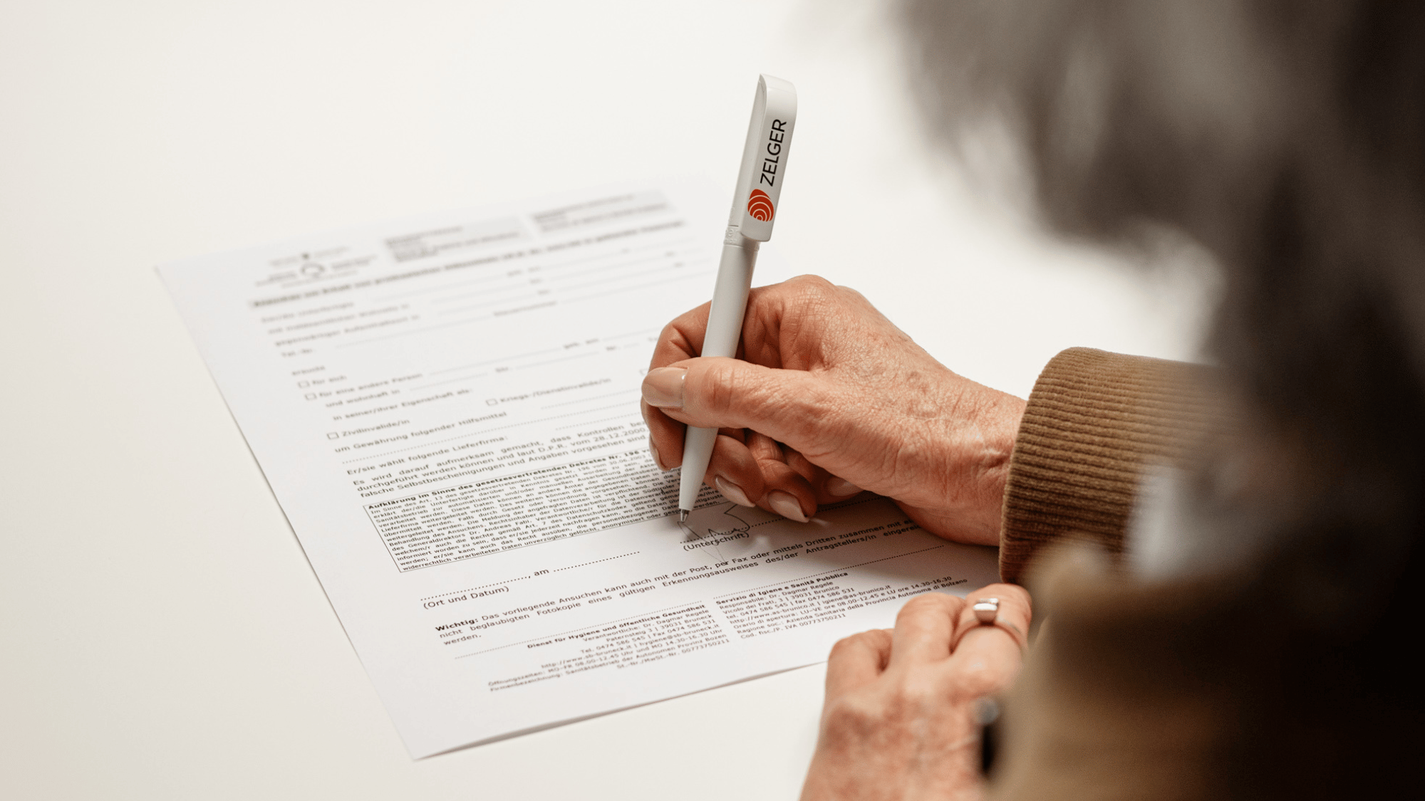 Cliente firma un modulo Zelger per la richiesta di contributi e agevolazioni sugli apparecchi acustici.
